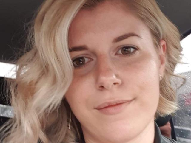 AnaysBigTits has blonde, wavy hair, brown eyes, and a slight smile with subtle makeup. She wears small earrings and a black top. Her nose is slightly freckled.