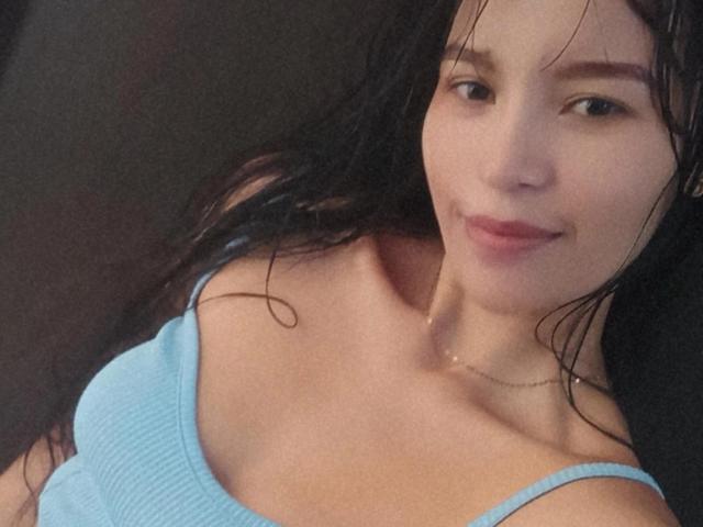 SusanKartier with wet black hair, light blue ribbed top, small tits, and a slight smile, showing a hint of her ass under the top. Her skin is fair.