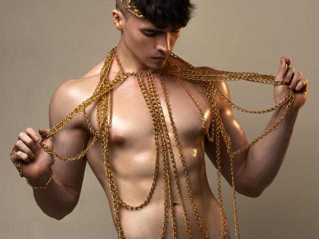 MiloLove, shirtless with a gold chain body harness, holding chains, muscular, brown hair, headpiece, looking down, beige background, shiny skin, toned abs, attractive, male, sexy.