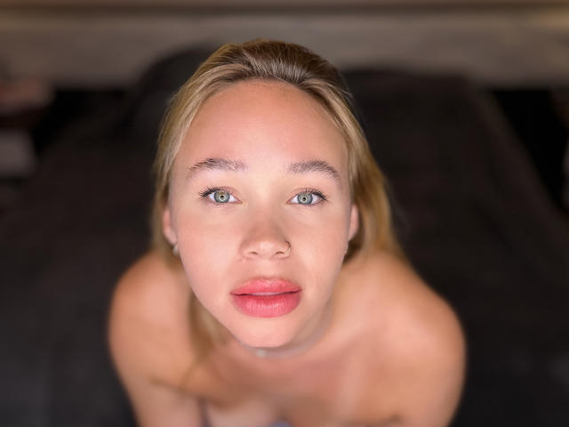VanillaCake has blue eyes, blonde hair, and pink lips. She's looking up with a slightly open mouth, and her bare shoulders are visible. Her tits are not shown.