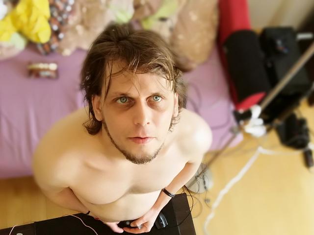 OndraSekCZech, shirtless, with wet brown hair, green eyes, and a beard, looking up, hands on black table, bare chest, and visible black belt in a bedroom.