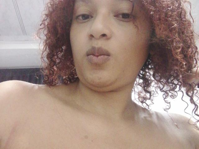 VioletaSwitch has curly red hair, light brown skin, and is pouting with her lips slightly pursed. She's topless, showing her bare shoulders and a small scar on her left.