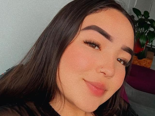 LilaRosa69 has a cute, smiling face with dark brown hair, a nose ring, and thick eyebrows. She's wearing a black sheer top, with pink lips and brown eyes.
