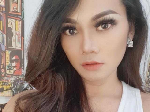 HugeCockJackie with long dark hair, thick eyebrows, long eyelashes, full pink lips, and a serious expression, wearing a white halter top, and diamond earrings.