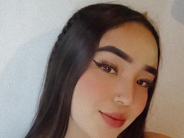 LilaRosa69 with long black hair, thick eyebrows, winged eyeliner, nose ring, and subtle smile, looking at camera, soft light, slightly pink cheeks, and subtle makeup.
