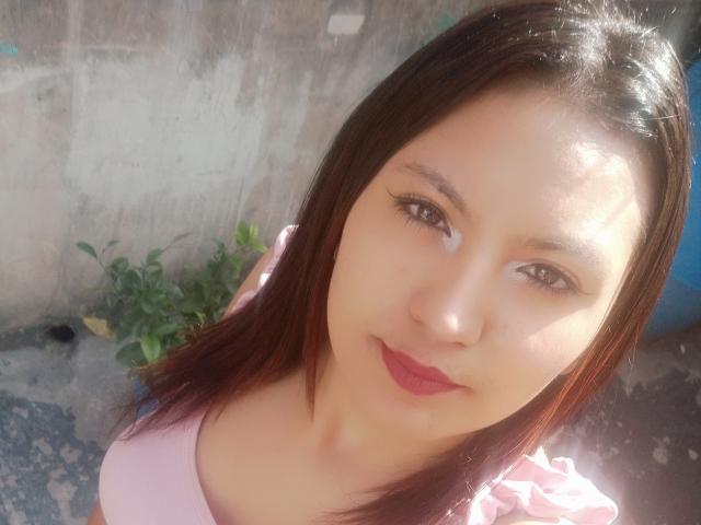 SalomeHottieX has light skin, brown eyes, and straight dark brown hair. She's wearing a pink top, with sunlit skin and pink lipstick. Her small tits are barely visible.