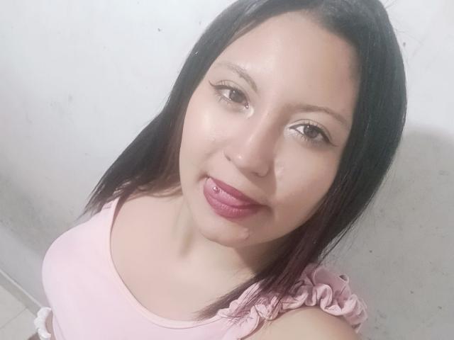 SalomeHottieX has light skin, dark straight hair, pink lipstick, and a lip piercing. She's wearing a pink top, showing small tits and a cute face.