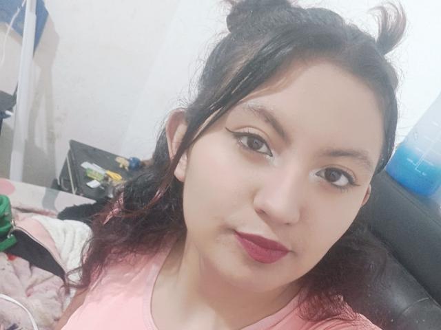 SalomeHottieX has dark hair in messy buns, pink shirt, red lipstick, and subtle eyeliner, with a slight smirk, looking at the camera. She's fair-skinned with a cute face.