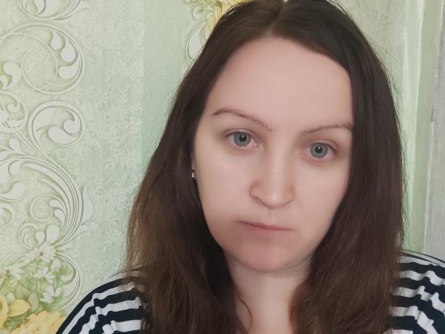 MillaOne has fair skin, green eyes, and brown wavy hair, wearing a striped shirt, with a neutral expression, looking slightly to the right.