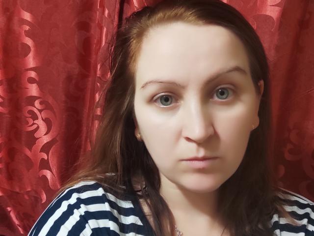 MillaOne has pale skin, green eyes, and brown hair. She's wearing a striped blue and white shirt. Her tits are small and she's looking straight at the camera.