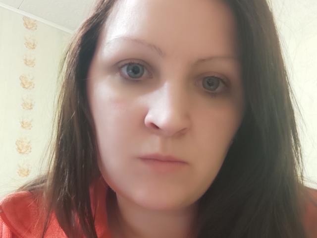 MillaOne has pale skin, blue eyes, and brown hair. She's wearing a red shirt with a serious, slightly pouty expression. Her face is centered, taking up most of the image.