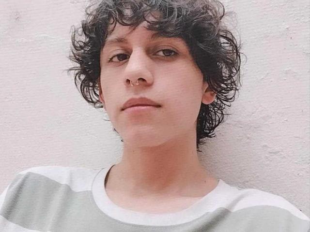  FelipeBrowns has curly black hair, a nose ring, and a neutral expression. He's wearing a gray and white striped shirt. His skin is light.