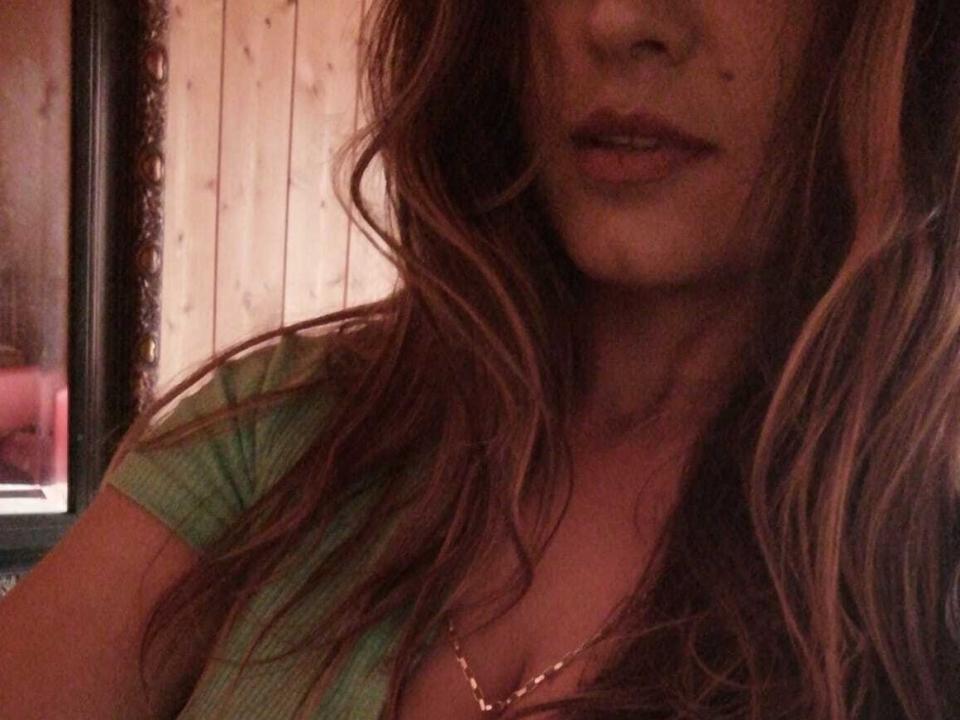 Hedua69's face and upper chest, showing wavy brown hair, green top, and a gold necklace, with her lips slightly open, revealing a hint of her tits.