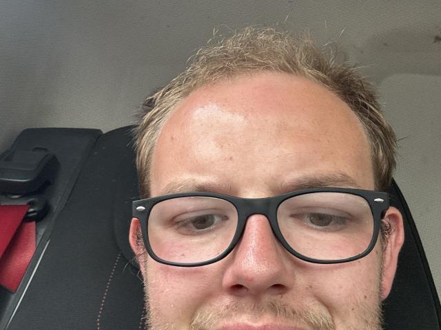 Beertjs has a balding head with blonde hair, black glasses, light brown eyes, and a slight beard. Red seat belt is visible on the left.