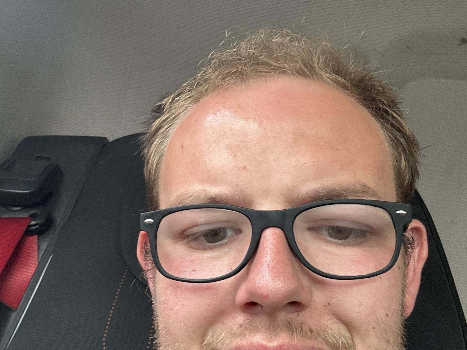 Beertjs has a balding head with blonde hair, black glasses, light brown eyes, and a slight beard. Red seat belt is visible on the left.