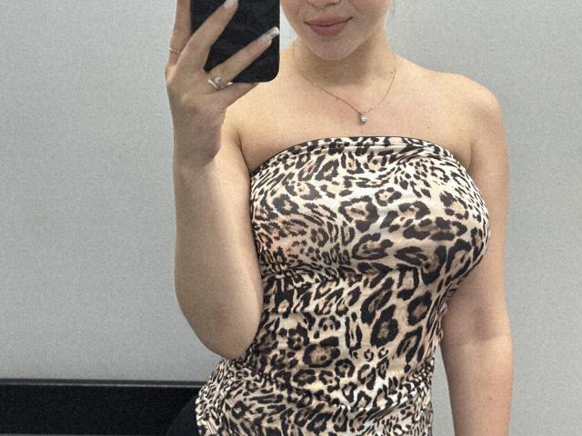 SugarrX has big, round tits in a strapless leopard print top, taking a mirror selfie with a smartphone, showing a subtle smile and a silver necklace.
