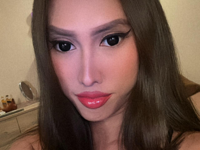 BombshellPh with glossy pink lips, thick black eyeliner, and long brown hair, staring directly at the camera, looking hot. Her ass is not visible in this shot.