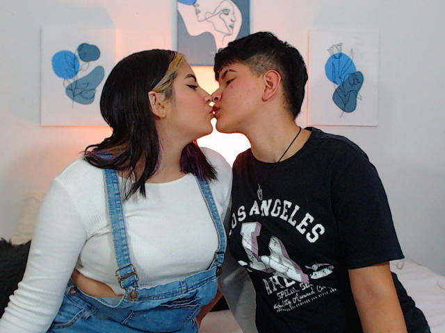 CamilleAndSophie, een mollige vrouw met zwart haar met paarse punten, een wit shirt en blauwe overalls, die een Aziatisch jongetje met kort haar in een zwart shirt met de tekst "Los Angeles" kust. Beide ogen zijn gesloten..