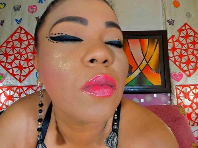Blacknestormmy has glossy pink lips, dark eyeliner with tiny black dots, and shiny skin. She's wearing a beaded necklace and has her eyes closed. Her hair is pulled back.