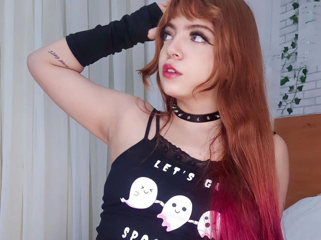 Acarolleao-hot with red-brown hair, black choker, and sleeve, wearing a ghost-print tank top, looking up, has a tattoo on her arm, and a nose ring.