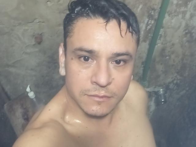 Santito has wet black hair, brown eyes, and a slightly chubby face with light skin, looking up at the camera, shirtless, with water droplets on his chest.