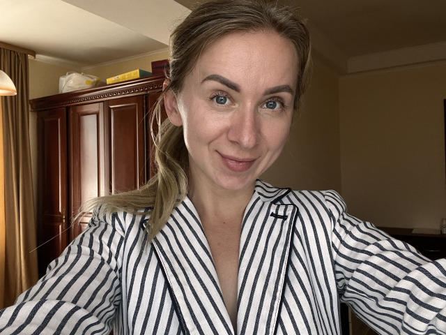 VasilisaSexy has blue eyes, a slight smile, and is wearing a striped black and white shirt. She's got blonde hair in a ponytail, and a cute, attractive face.