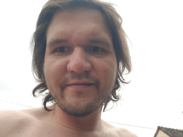NectarineFad, shirtless with medium-length brown hair, a slight beard, and a small nose, smiling slightly. His face is centered, with a white background.