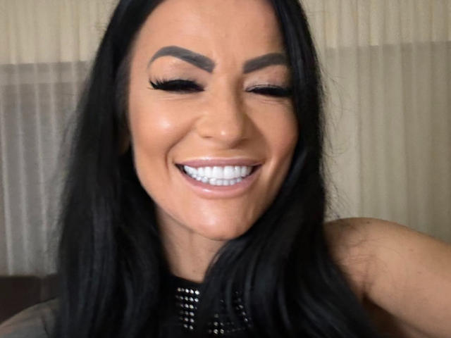 AndraD's smiling face with closed eyes, dark eyebrows, long black hair, and shiny white teeth. She's wearing a black top with a mesh neckline.
