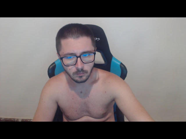 Shirtless ChanceOfGod with glasses, short brown hair, and a beard, sitting in a blue and black gaming chair, looking down with a neutral expression.