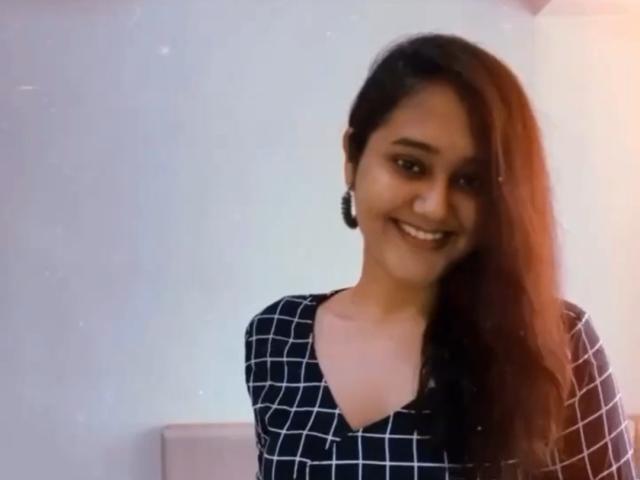 Rosysona tem a pele morena, cabelos longos ruivo-laranja, brincos pretos e uma blusa preta xadrez. Ela está sorrindo, mostrando os dentes, com uma aparência fofa e sexy..