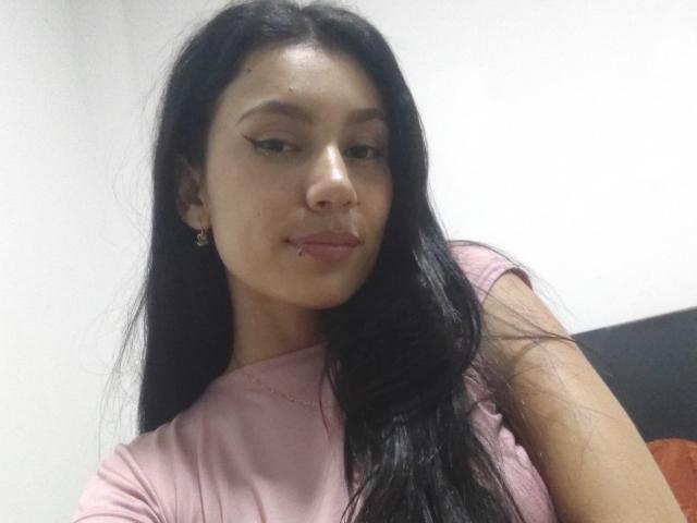 KataleyaMansson has long black hair, light brown skin, and a nose piercing. She's wearing a pink shirt with winged eyeliner, and a small earring is visible.