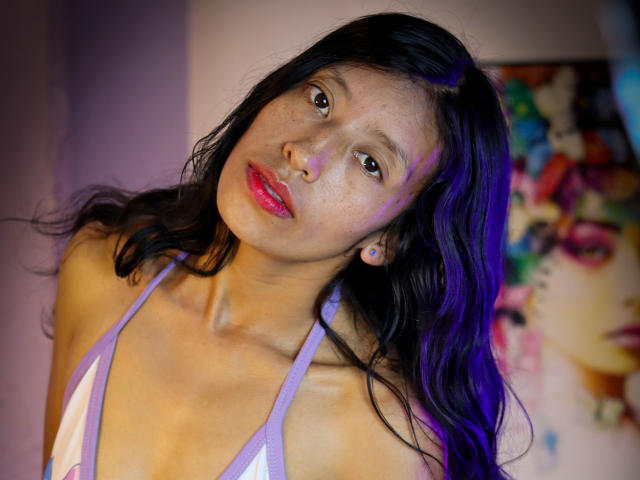 KarolineS with dark wet hair, purple lit face, red lipstick, freckles, and white-purple bikini top, looking up with a slightly tilted head. Her tits are small and visible.