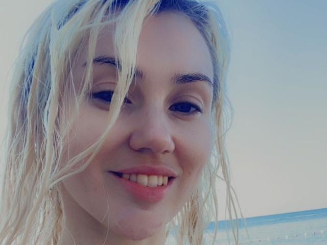 MoonBabeX has blonde, wet hair, light skin, and a small, cute nose with a subtle smile showing straight teeth. Her eyes are slightly squinted, and she's looking at the camera.