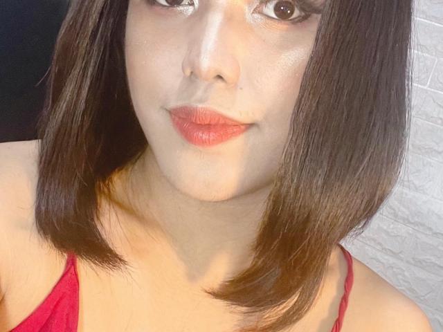 Chelsealou69 with straight brown bob, red lipstick, shiny skin, and red spaghetti straps, showing her pouty lips and small nose. Her tits are not visible in the image.