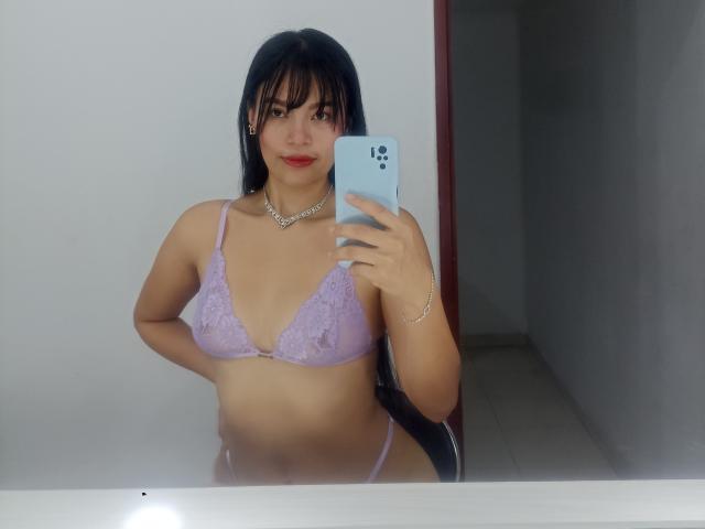SusanKartier with long black hair, wearing a lilac lace bra and matching panties, holding a blue phone, showing her boobs, red lipstick, and a silver necklace in a mirror selfie.