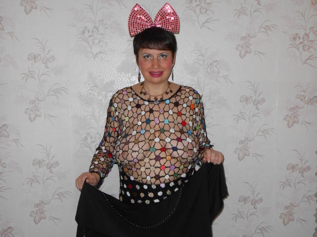 AirMagdalene, con cabello corto y castaño, un lazo rojo con lunares, vistiendo una blusa de malla transparente con patrones de estrellas de colores, que deja ver sus pechos, y sosteniendo una falda negra..