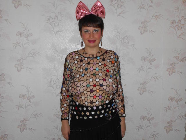 AirMagdalene, avec ses courts cheveux noirs, un nœud rouge à pois, un haut noir transparent qui révèle ses seins, des motifs d'étoiles colorés, une jupe noire et une ceinture à chaîne, souriant à l'appareil photo..