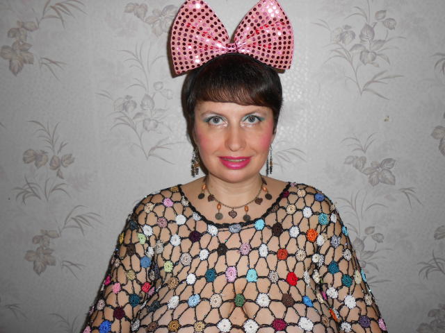 AirMagdalene con cabello castaño oscuro, un lazo rosa con lunares, y un top de malla de colores, mostrando sus pechos a través de la malla, llevando un collar y pintalabios rosa..