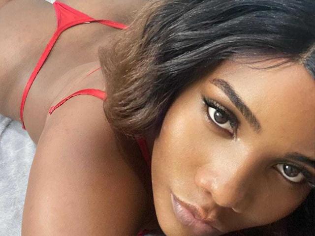 SamiiaSmith lying on her stomach, wearing a red thong, showing her butt, with dark brown hair and brown eyes, looking at the camera with a slight smile.