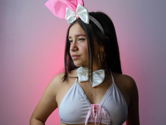 LilithSwett with pink bunny ears, white bow, and choker, wearing a grey bikini top, showing her tits, looking side, with pink and white lighting.