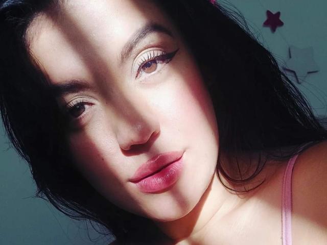 LauraRichis has light skin, black hair, and pink lipstick, with sunlight highlighting her face, showing her eyeliner, and pink tank top. Her ass is not visible.