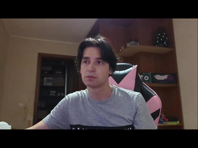 BarryAllen, a dude with dark, wavy hair and a medium build, wearing a gray shirt, sits in a pink and black chair, looking serious.
