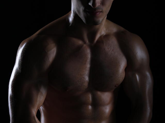 La poitrine et les bras musclés et brillants d'AdamTasty ressortent sur un fond sombre. Ses abdominaux et ses pectoraux bien définis brillent, mettant en valeur sa silhouette forte, sexy et transpirante..