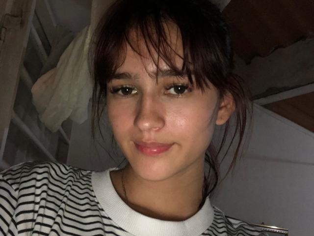 MelodyMansson has dark brown eyes, a small nose, and a subtle smile with slightly shiny skin, wearing a striped shirt, and has her hair in a messy ponytail.
