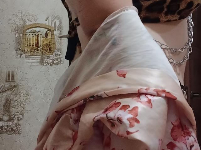 DiLaria's ass, covered in a silky white and pink floral dress, with a chain and leopard print top. Her skin is pale, and the image focuses on her backside.