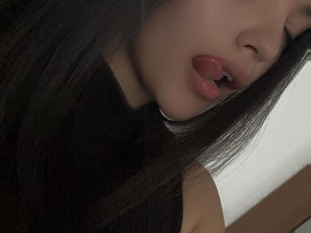 IssaPuasini's face is in the frame with her tongue slightly out, lips parted, wearing a black sleeveless top, long dark hair covering part of her face.
