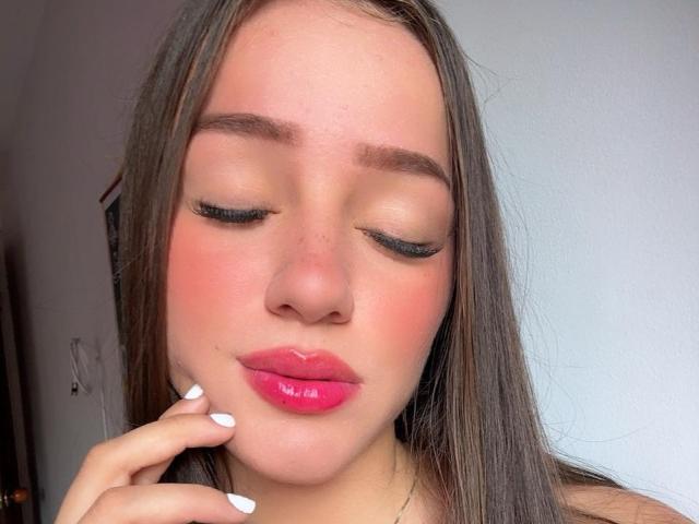 Antonia Sanchez, con labbra rosa e lucide, naso leggermente all'insù, sopracciglia marroni, occhi chiusi con lunghe ciglia nere, che tocca il mento con le dita dalle unghie bianche, capelli castani e lisci..