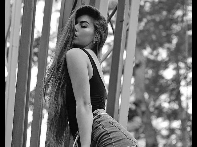 StellaBeckker's face, black hair, brown eyes, black eyeliner, nose piercing, septum ring, tongue out, tongue piercing, light skin, choker necklace, looking at camera, slightly open mouth.