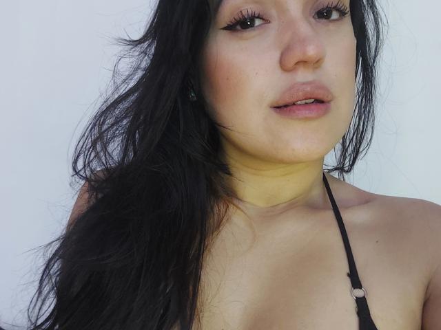 LauraRichis with long black hair, eyeliner, and parted lips, wearing a black halter top, exposing her shoulders and upper chest. Her yellow neck chafing is visible.