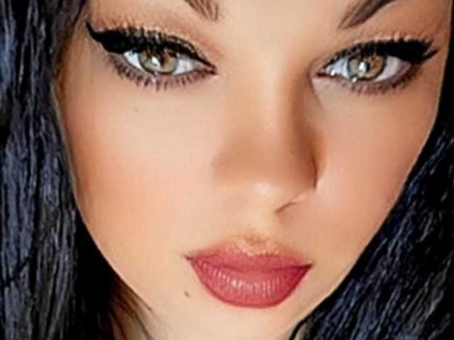 SweettM hat ein attraktives Gesicht mit braunen Augen, dicker schwarzer Eyeliner, rotem Lippenstift und dunklem, glattem Haar. Sie blickt direkt in die Kamera mit leicht geöffneten, vollen, roten Lippen..